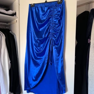 Blå satinkjol från - Snygg blå satinkjol med en trendig snörning på framsidan. Kjolen har en elegant glans och en smickrande passform som gör den perfekt för speciella tillfällen. Den elastiska midjan ger extra komfort och stil. Använd en handfull gånger. Önskar du veta exakta mått? Tveka inte att höra av dig!💙