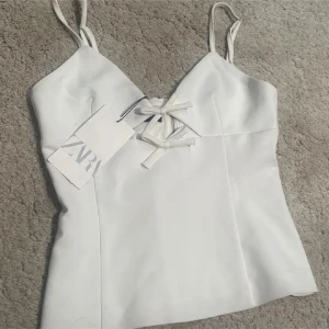 Vit korsettopp från Zara - Säljer en stilren vit korsettopp från Zara med smala axelband och snygg snörning framtill. Perfekt för en chic look.