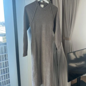 Beige stickad klänning - Säljer en mysig beige stickad klänning med långa ärmar och ribbad halsringning. Perfekt för kyligare dagar och ger en stilren look. Passar bra till både vardag och mer uppklädda tillfällen.