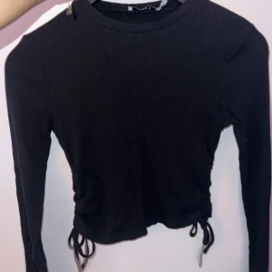 Svart ribbad tröja med knyt - Snygg svart ribbad tröja med långa ärmar och knyt i sidorna. Perfekt för en stilren look. Från NA-KD. 