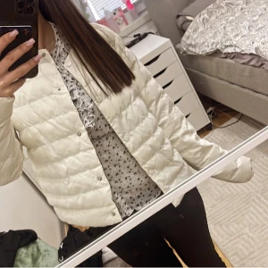 Vit quiltad jacka - Säljer en stilren vit quiltad jacka med knappar. Jackan har en normal passform och är perfekt för kyligare dagar. Den är långärmad och har en enkel design som gör den lätt att matcha med olika outfits. Trots att den ser tunn ut så blir man så himla varm!! Verkligen en allväder jacka!!!