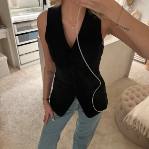 Kostymväst från H&M - Svart väst med knappar framtill. Perfekt för en stilren look. Västen har en design med en v-ringad hals och är från H&M