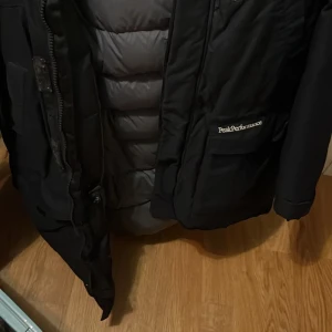 Svart dunjacka från Peak Performance - Säljer en svart dunjacka från Peak Performance. Jackan har en dragkedja framtill och flera praktiska fickor. Perfekt för kyliga dagar med sin varma vaddering. En stilren och funktionell jacka för vintern.köpt för 3800kr från stadium jätte varm 