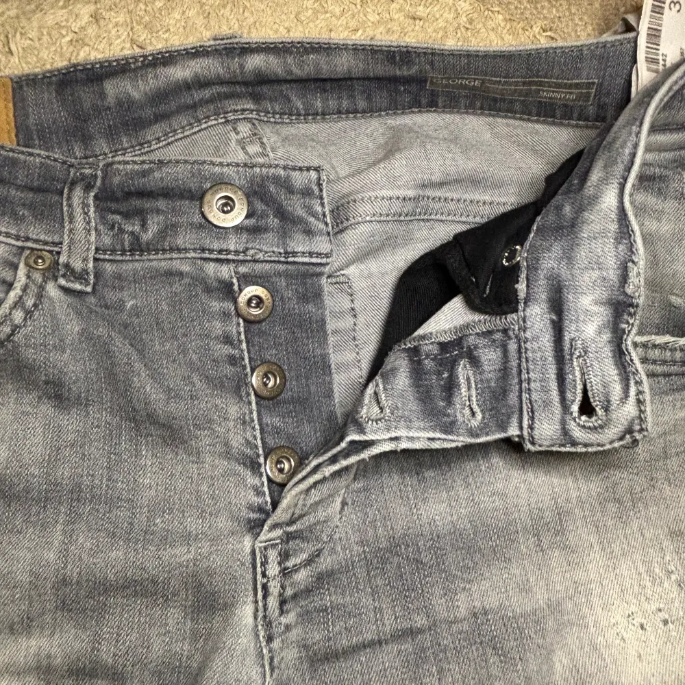 Grå Dondup jeans i George modellen, alla slitningar är orginal. Dåliga är att D:et som ska vara på bakfickan har gått av. Priset är satt baserat på det. Hör gärna av dig om det är något du funderar över. Leon. Farkut & Housut.