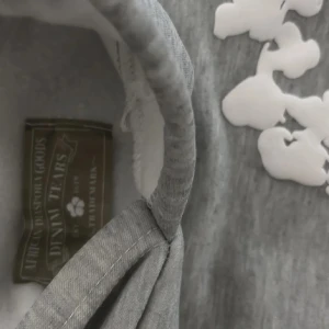 Grå Denim Tears hoodie - Säljer en grå hoodie från Denim Tears med ett unikt vitt blommönster över hela tröjan. Den har en klassisk känguruficka och en bekväm huva. Perfekt för en avslappnad stil.