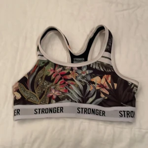 Blommig sporttopp från Stronger - Snygg sporttopp från Stronger med ett färgglatt blommönster. Toppen har en elastisk kant med logotypen 'STRONGER' och är tillverkad i en blandning av polyester och spandex för en bekväm passform. 