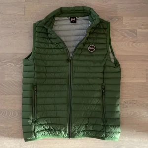 Grön dunväst från Colmar - Säljer en snygg grön dunväst från Colmar. Västen har en dragkedja framtill och två praktiska fickor med dragkedjor. Perfekt för kyligare dagar och ger en stilren look. Passar S/XS. Perfekt för våren. Tveka inte på att höra av er för ytterligare frågor. 