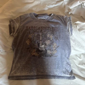 Grå t-shirt från Zadig & Voltaire - Jag säljer en fin grå t-shirt från Zadig & Voltaire med tryck av en gitarr och blommor. Tröjan är i ganska bra sick💕man kan tyvärr ej skicka tillbaka tröjan 💕
