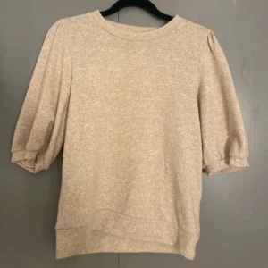 Beige tröja med trekvartsärm - Säljer en stilren beige tröja med trekvartsärm. Perfekt för en avslappnad look. Tröjan har en rund hals och är tillverkad i ett mjukt material som ger en bekväm passform.