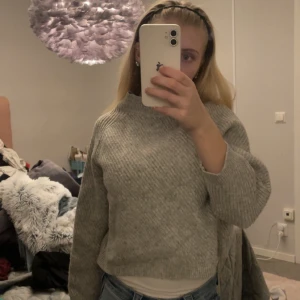 Grå stickad tröja från MNG Basics - Säljer en mysig grå stickad tröja från MNG Basics i ullblandning. Tröjan har en ribbad struktur och långa ärmar, perfekt för kyligare dagar. Den är enkel att matcha med olika outfits och ger en stilren look, kortare modell i armarna och vid magen. Ganska liten i storleken 