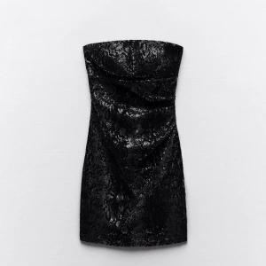 Svart axelbandslös klänning - Snygg svart axelbandslös klänning med glittrigt mönster. Perfekt för en kväll ute eller en speciell tillställning. Klänningen har en elegant passform som framhäver figuren.