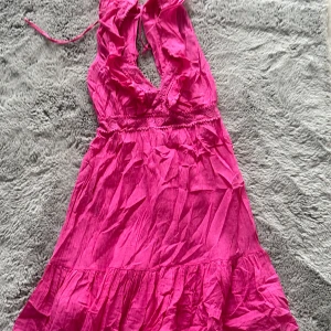 Rosa klänning med volangdetaljer - Snygg rosa klänning med volangdetaljer och knytning i nacken. Perfekt för sommarens festligheter med sin livfulla färg och feminina stil.