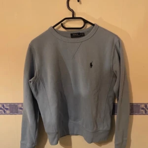 Blå tröja från Polo Ralph Lauren - Säljer en stilren blå tröja från Polo Ralph Lauren med deras ikoniska logga broderad på bröstet. Tröjan har långa ärmar och en rund halsringning. Perfekt för en avslappnad och snygg look. Storlek s dam