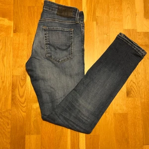 Blå slim jeans från Jack & Jones - Snygga blå slim jeans från Jack & Jones, modell Glenn. Perfekta för en stilren look med klassisk femficksdesign och knappgylf. Passar utmärkt till både vardag och mer uppklädda tillfällen. Skriv vid funderingar.