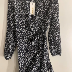 Blommig omlottklänning från ONLY - Supersöt marinblå omlottklänning från ONLY med vitt blommönster. Klänningen har lång ärm, knyt i midjan och. Perfekt för vår och sommar! 🌸