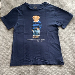 Blå t-shirt med Polo Bear från Ralph Lauren - Säljer en snygg blå t-shirt från Ralph Lauren med det ikoniska Polo Bear-motivet på framsidan. T-shirten är kortärmad och tillverkad i mjuk bomull. Använd ett väldigt fåtal gånger. |nypris:695|Storlek S|🐻💙