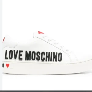 Vita sneakers från Love Moschino - Säljer ett par vita sneakers från Love Moschino med svart logotyp på sidan och en liten röd hjärtdetalj vid hälen. Skorna har klassisk snörning och en stilren design som sticker ut. Kom privat för egna bilder🥰🥹🫰🏽❤️
