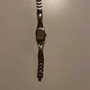 Silverfärgad armbandsklocka från DKNY - Säljer en stilren armbandsklocka från DKNY i silverfärgat metall med elegant, tvinnad länkdesign. Klockan har en rektangulär urtavla och passar perfekt som accessoar till olika tillfällen.Är litet runt hand vristen.Behövs ett nytt batteri 