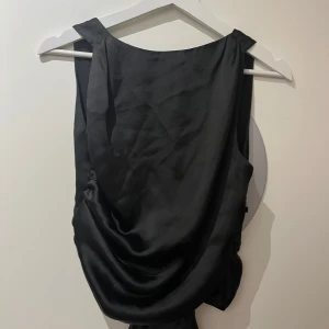 Svart satinlinnetopp från Zara - Säljer en svart linnetopp i satin från Zara. Toppen har en snygg draperad framsida och knytning i ryggen för en snygg passform. Storlek M men skulle säga att den även passar S 