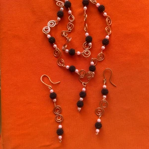 Handgjort halsband och örhängen med pärlor och koppartråd - Unikt set med halsband och matchande örhängen i snirklig koppartråd, dekorerade med svarta och rosa pärlor. Perfekt för dig som vill sticka ut med ett personligt smycke.