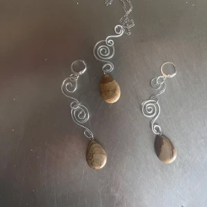 Handgjorda örhängen och halsband med brun sten - Unika smycken med virad silverfärgad metalltråd och droppformad brun sten. Setet består av ett halsband och ett par matchande örhängen med vackra mönster i stenen.