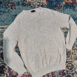 Ljusgrå v-ringad tröja i pima cotton - Säljer en stilren ljusgrå v-ringad tröja i mjuk pima cotton. Tröjan har långa ärmar, ribbade muddar och en klassisk passform som funkar till många tillfällen. Perfekt för lager-på-lager eller som den är.