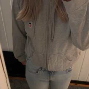 Grå hoodie från Iconic Sport - Säljer en grå hoodie från Iconic Sport i storlek medium. Tröjan har dragkedja framtill, huva med snören och en liten broderad logga på bröstet. Perfekt för en avslappnad stil.