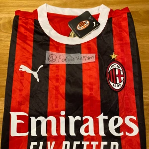 AC Milan hemmatröja Puma - Säljer en klassisk AC Milan hemmatröja från Puma med röd och svart randigt mönster, vit krage och detaljer. Tröjan har klubbmärke och Puma-logga på bröstet samt sponsortryck framtill. Perfekt för dig som älskar italiensk fotboll.