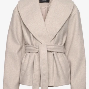 Beige kappa från Vero Moda - Snygg beige kappa från Vero Moda med ett brett bälte i midjan och stora slag. Jackan har en elegant design med långa ärmar och en mjuk, ullig känsla. Perfekt för kyligare dagar.