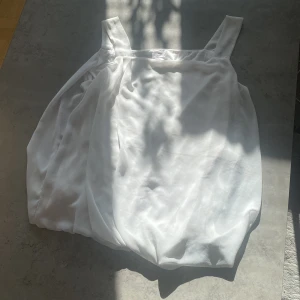 Vit ärmlös topp från Stockholm - Säljer en stilren vit ärmlös topp från Stockholm. Toppen har breda axelband och är tillverkad i ett lätt och luftigt material, perfekt för varma dagar. Passar bra till både jeans och kjol. Perfekt för en somrig look! 🌞