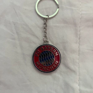 FC Bayern München nyckelring - Säljer en rund nyckelring med FC Bayern München-logga. Nyckelringen har röd kant, silverfärgad metall och blå-vita detaljer i mitten. Perfekt accessoar för fotbollsfans!