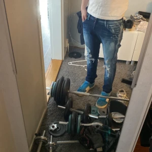 Blå slitna jeans från Replay  - Säljer ett par blå jeans från Replay, modell Pilar. Jeansen har slitna detaljer och hål på benen, knappar i gylfen och klassiska bakfickor. Snygg tvätt och relaxed vibe, perfekta till sneakers. Storleken är mer som 29 31 typ