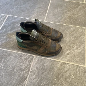 Valentino Rockrunner sneakers i camouflage - Säljer ett par Valentino Rockrunner sneakers med klassiskt camouflage-mönster i gröna och bruna toner. Skorna har snörning, rund tå och detaljer i skinn och mocka samt en mintgrön häl. Perfekta för en stilren look! Nypris ca 7000 mitt pris 1199