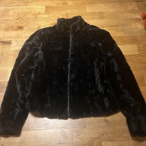 Svart fuskpälsjacka från Pull&Bear - Säljer en svart fuskpälsjacka från Pull&Bear i storlek M. Jackan har hög krage och stängs med dragkedja framtill. Perfekt för dig som vill ha en mjuk och stilren jacka med lite lyxig känsla.