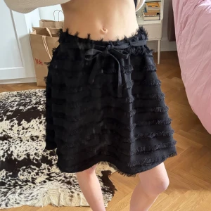 Svart kjol med fransar - Svart kjol med jättefina detaljer i form av fransar och även ett band att knyta i midjan! Köpt på H&M, använd endast en gång. Storlek 34 men passar på mig som vanligtvis har storlek 36/38🖤 200 kr + frakt