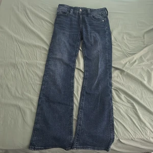 Blå jeans från Gina Tricot - Snygga blå jeans från Gina Tricot med en klassisk femficksdesign. Byxorna har en bootcut-stil och är perfekta för en avslappnad look. De är tillverkade i ett bekvämt denimtyg och har en knapp- och dragkedjestängning framtill.