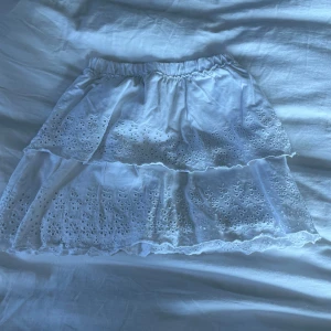Vit kjol från Zara - Säljer en söt vit kjol från Zara med broderade detaljer. Kjolen har en elastisk midja och två lager med volanger som ger en fin volym. Perfekt för varma dagar!