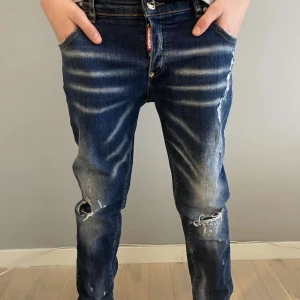 Blå slitna jeans från Dsquared2 - Säljer ett par blå jeans från Dsquared2 med slitningar och hål på knäna. Jeansen har slim passform, klassisk femficksdesign och tydliga slitdetaljer framtill. Perfekta för en avslappnad och trendig look.