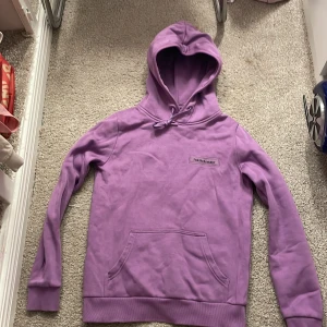 Lila hoodie från Peak Performance - Säljer en snygg lila hoodie från Peak Performance. Den har en klassisk design med en stor ficka framtill och justerbar huva. Perfekt för en avslappnad stil.