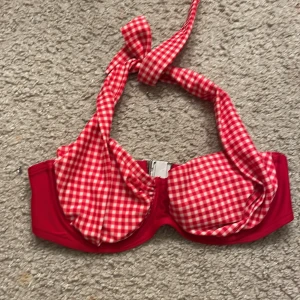 Röd och vit rutig bikiniöverdel från Abecita - Snygg bikiniöverdel från Abecita i röd och vit rutig design. Den har en knytning i nacken och en stadig bygel för extra stöd. Perfekt för en dag på stranden eller vid poolen.