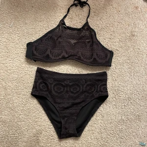 Svart spetsbikini från Cubus - Snygg svart bikini från Cubus med spetsdetaljer. Toppen har en hög hals och knytning i nacken. Bikinin är perfekt för en stilren look på stranden.