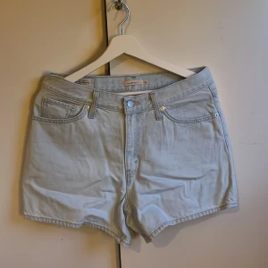Ljusblå jeansshorts från Levi's - Säljer ett par snygga ljusblå jeansshorts från Levi's. De har en klassisk 80-tals mom fit med fem fickor och knappgylf. Perfekta för en avslappnad sommarlook. 🩳Endast använda en gång. Är äkta, köpt från Levi’s store‼️‼️