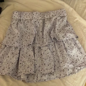 Blommig kjol från Name It - Söt blommig kjol från Name It i lila och vita toner. Kjolen har volanger och ett elastiskt midjeband för bekväm passform. Perfekt för en somrig look!