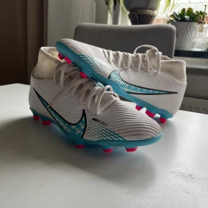 Vita Nike Mercurial fotbollsskor - Säljer ett par vita Nike Mercurial fotbollsskor med blå och svarta detaljer. Mycket bra skick knappt använda lite smutsiga vid srumpan. Storlek 42 priset diskuteras 