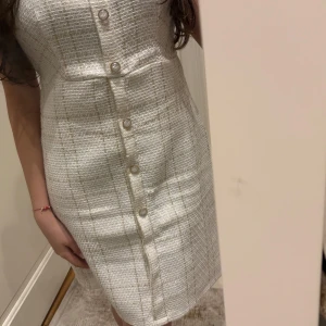 Vit klänning med matchande jacka och pärlknappar - Säljer en elegant vit klänning i strukturerat tyg med raka linjer och pärlknappar framtill. Klänningen har en figurnära passform och matchas med en kort jacka i samma material. Perfekt för vår eller sommar.