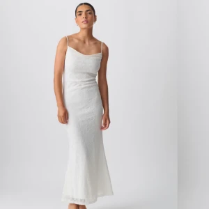 Vit långklänning med spets och smala axelband - Elegant vit långklänning med smala axelband och vacker spets över hela klänningen. Klänningen har en figurnära passform och öppen rygg med knytning. Helt oanvänd med prislappen kvar! Nypris 599kr men säljer för 300kr!