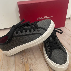 Salvatore Ferragamo Sneakers, Grå/Svarta, EUR 43 - Ett par stilrena sneakers från Salvatore Ferragamo. Skorna har en mörkgrå färg med ett mönster. Perfekt för en avslappnad men sofistikerad look.  Storlek: 8/M/43 Skick: 9/10  Använda en gång. Kommer med box och dustbags
