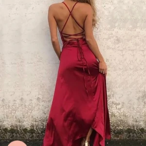 Röd balklänning med öppen rygg och snörning - Säljer en elegant röd balklänning i satin med smala axelband som korsas i ryggen och snörningsdetalj. Klänningen har en v-ringad front. Jag är 168 lång och den är uppsydd för att passa min längd så skulle säga att den passar mellan 166-174 cm. Är man kortare kan man sy upp mer. Den är endast använd en gång så super fint skick, nypris är ca 1300kr då frakten kostade 400kr. 