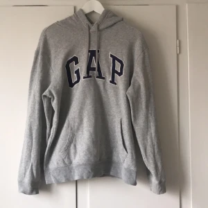 Grå hoodie från GAP - Säljer en klassisk grå hoodie från GAP. Tröjan har en bekväm passform med långa ärmar och en praktisk magficka. Perfekt för en avslappnad stil. Passar både kvinnor & män. Strl M.