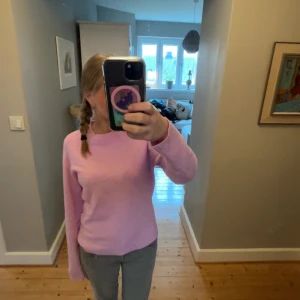 Ljusrosa stickad tröja - Mysig ljusrosa stickad tröja med rund halsringning och långa ärmar. Tröjan har en enkel och klassisk design med ribbade muddar vid ärmslut och nederkant. Perfekt för lager-på-lager och passar till det mesta. 